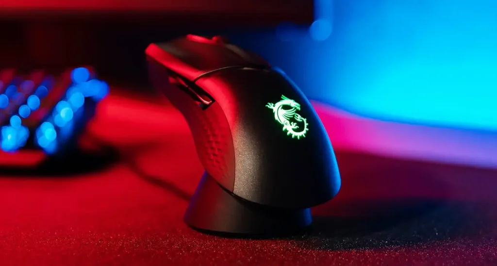 A black MSI Clutch GM31 wireless gaming mouse sits on a dark surface. The mouse has a sleek design with subtle angles and a glowing MSI logo on the back. This is highlighted as a strong contender for the best budget wireless gaming mouse due to its included charging dock.