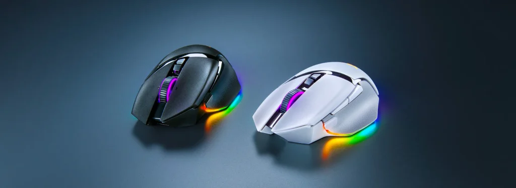 Two Razer Basilisk V3 Pro wireless gaming m ice, one black and one white, are positioned on a dark, reflective surface with colorful RGB lighting emanating from their bases.